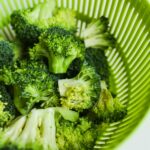 Fresh cut broccoli florets placed in a green colander, highlighting vibrant colors and freshness.