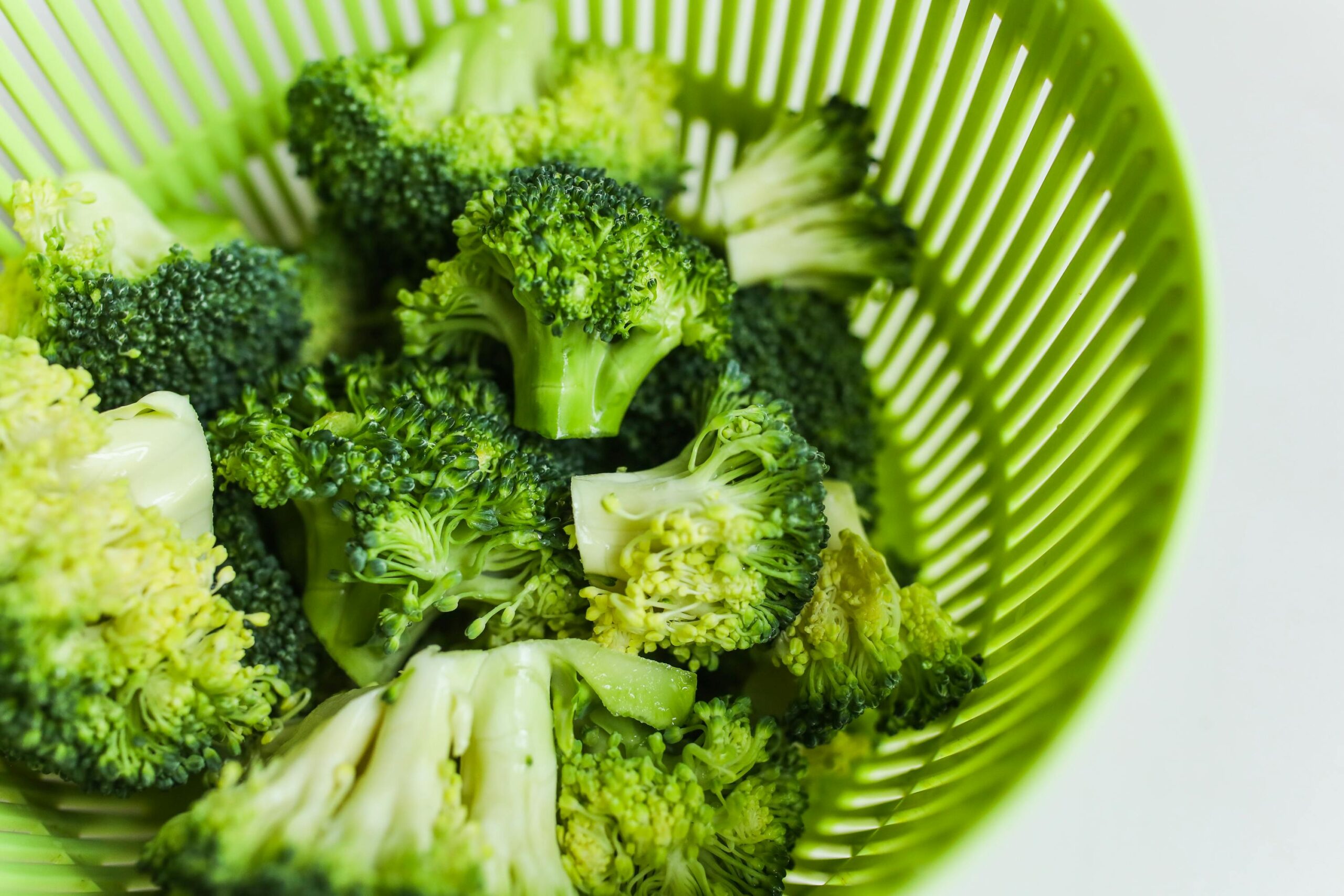 Fresh cut broccoli florets placed in a green colander, highlighting vibrant colors and freshness.